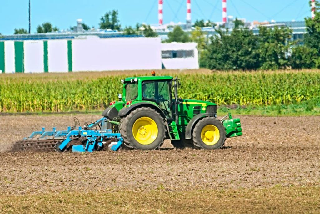 Green tractor plowing a field under a blue sky